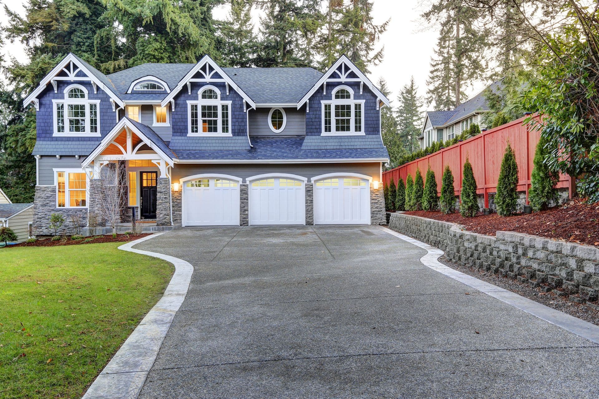 Charming two-story house with blue-gray siding, white trim, and large windows. Three-car garage, spacious driveway, and manicured garden.